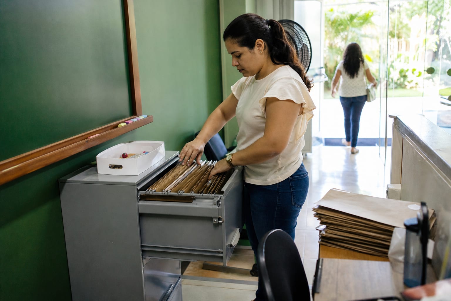 Funcionária organiza pastas de matrícula em arquivo de aço na secretaria da escola